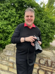 Ein Foto aus der Situation heraus, von einer Kundin fotografiert, es zeigt mich Thomas Schoo Business Fotograf Münster mit Wohnort Ochtrup im neuen Businessoutfit – einem schwarzen Pullover und rotem Polo-Shirt, abgerundet mit schwarzer Hose! Authentisch mit Kamera in der Hand, das Bild REAL und unbearbeitet.