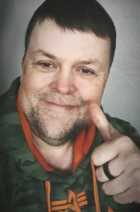 Ein typisches Selfie von mir im Urban-Style mit 3-Tage-Bart und einem Hoddie im Tarnfleckenlook, dazu ein lässiger Blick und Daumen hoch! Das war mein Look als Business Fotografen im Münsterland bis 2024.