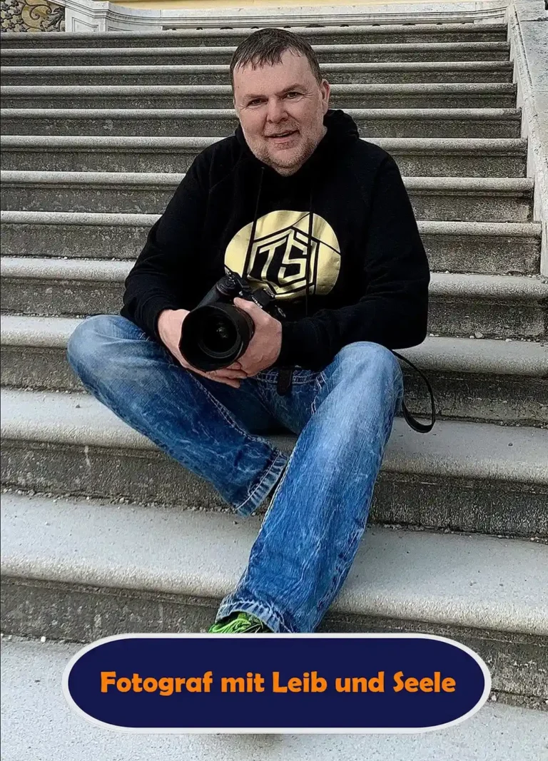 Fotograf Thomas Schoo im schwarzen Hoodie mit goldenem Logo, blauer Jeans und Kamera in den Händen sitzt auf einer Steintreppe am Schloss Schönbrunn in Wien – Kurzporträt mit einem dunkelblauen Button und orangefarbener Schrift: „Fotograf mit Leib und Seele