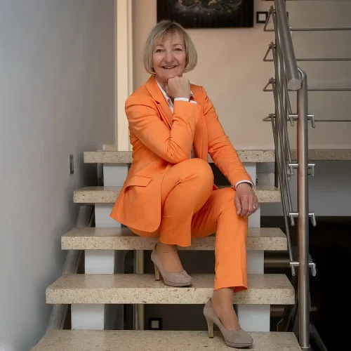 Business-Coach Sabine Wehrhahn im orangefarbenen Anzug auf einer Treppe – fotografiert von Personal Branding Fotograf Thomas Schoo bei einem Homeshooting in Hannover.