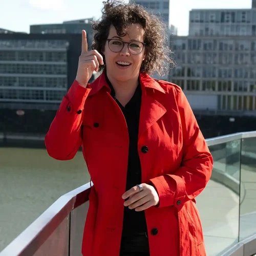 Human Design Coach Anika Wendling im roten Mantel mit erhobenem Zeigefinger – fotografiert von Personal Branding Fotograf Thomas Schoo im Medienhafen Düsseldorf.
